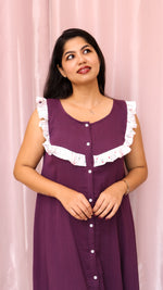 Woman wearing a purple dress with white ruffled details against a pink curtain background