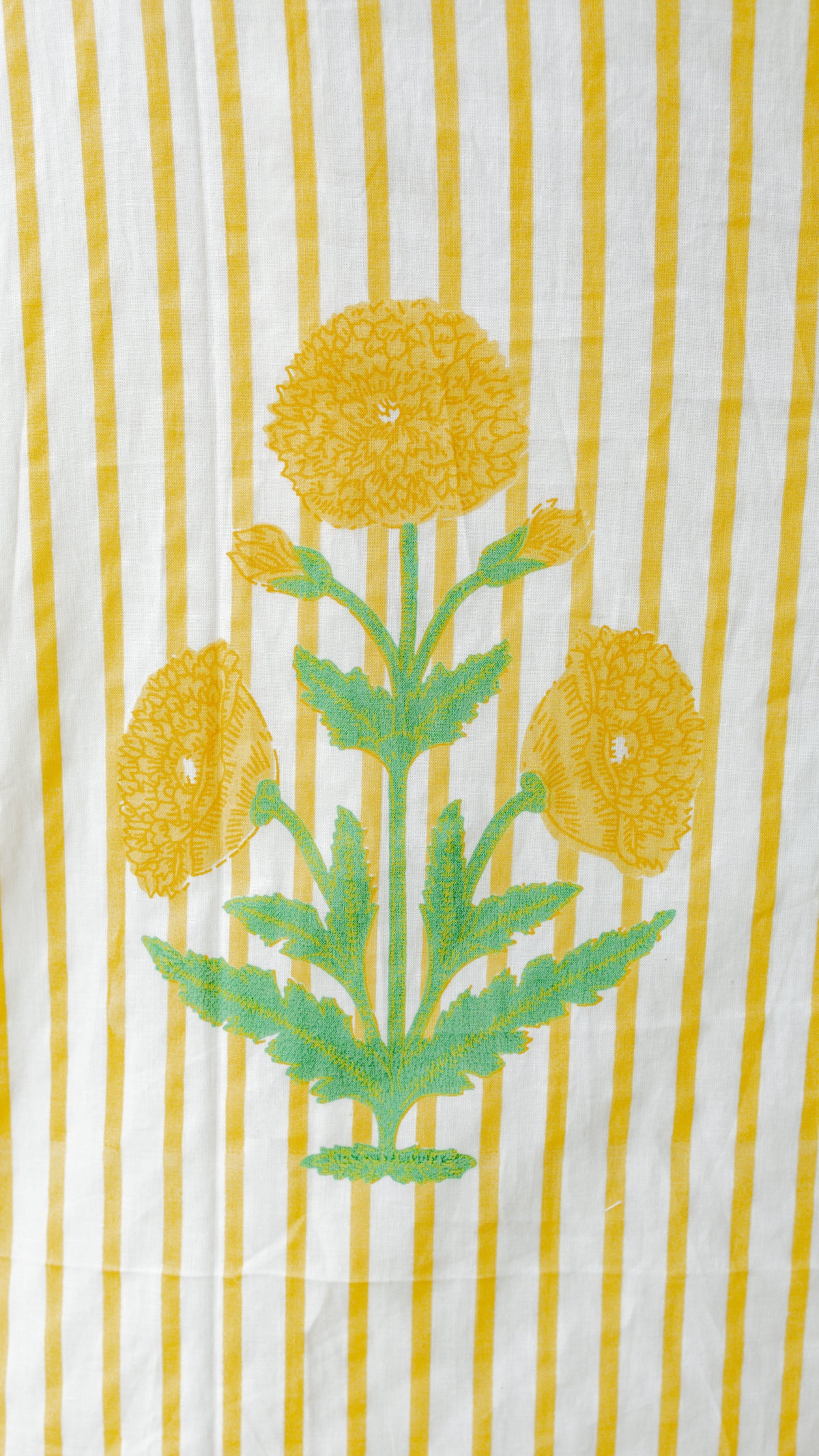 A close-up of a striped textile featuring vertical yellow and white stripes with a central green and yellow floral print.